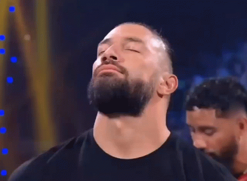 A Man With A Beard Is Standing In A Dark Room With His Eyes Closed And His Mouth Open . GIF