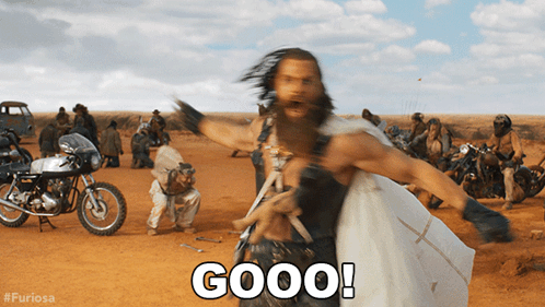 A Man With A Beard Is Standing In A Dirt Field With Motorcycles And Says Good GIF
