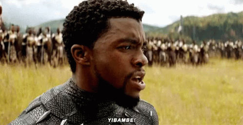 A Man With A Beard Is Standing In A Field With A Crowd Of People Behind Him And Says Yibambo ! GIF