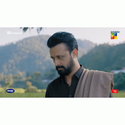 a man with a beard is standing in a field with mountains in the background and a advertisement for itel on the bottom ri