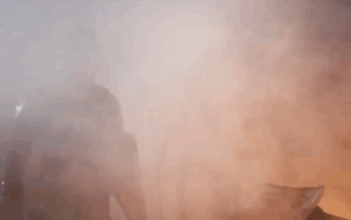 A Man With A Beard Is Standing In A Foggy Room With His Hands Outstretched . GIF