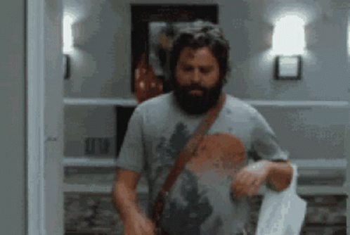 A Man With A Beard Is Standing In A Hallway Holding A Towel GIF