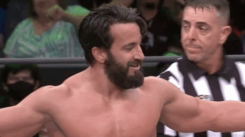 A Man With A Beard Is Standing In A Ring With A Referee . GIF