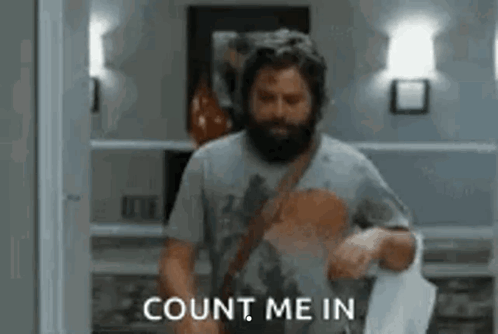 A Man With A Beard Is Standing In A Room Holding A Piece Of Paper . GIF