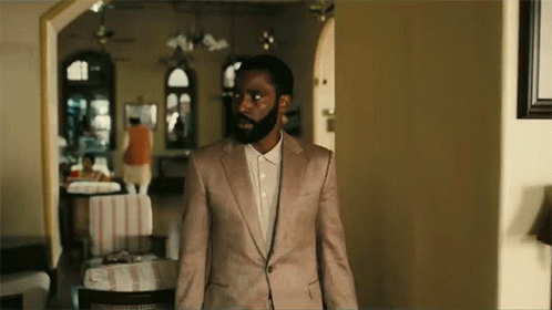 A Man With A Beard Is Standing In A Room Wearing A Pink Suit And White Shirt . GIF