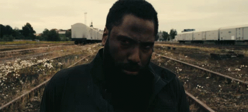 A Man With A Beard Is Standing In A Train Yard GIF