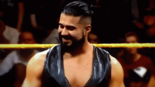 A Man With A Beard Is Standing In A Wrestling Ring And Smiling At The Camera . GIF