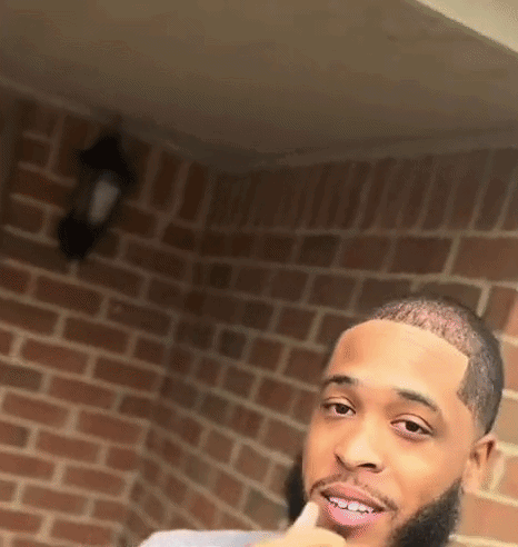 A Man With A Beard Is Standing In Front Of A Brick Wall . GIF