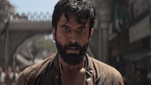 A Man With A Beard Is Standing In Front Of A Bridge GIF