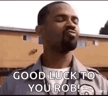 A Man With A Beard Is Standing In Front Of A Building With His Eyes Closed And Says `` Good Luck To You Rob '' . GIF