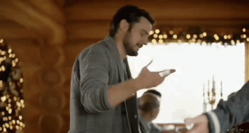 A Man With A Beard Is Standing In Front Of A Christmas Tree In A Cabin . GIF