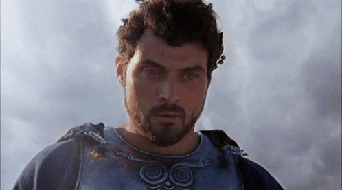 A Man With A Beard Is Standing In Front Of A Cloudy Sky And Looking At The Camera . GIF