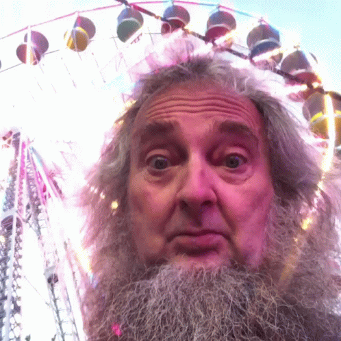 A Man With A Beard Is Standing In Front Of A Colorful Ferris Wheel GIF