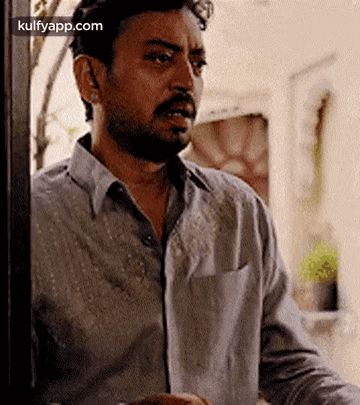 A Man With A Beard Is Standing In Front Of A Door And Looking Out . GIF