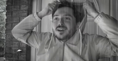 A Man With A Beard Is Standing In Front Of A Door With His Jacket On GIF