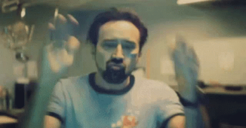 A Man With A Beard Is Standing In Front Of A Glass Door With His Hands Behind It . GIF