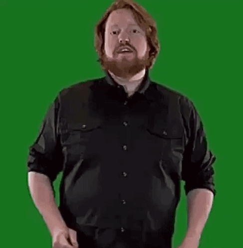 A Man With A Beard Is Standing In Front Of A Green Screen Holding A Large Letter B . GIF