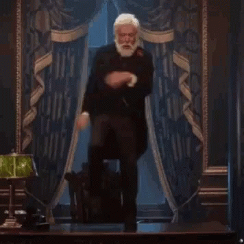 A Man With A Beard Is Standing In Front Of A Lamp In A Room . GIF