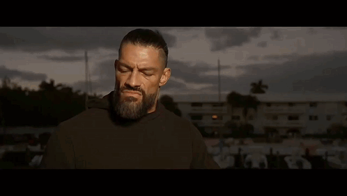 A Man With A Beard Is Standing In Front Of A Man With His Hands Folded . GIF