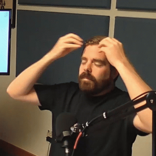 A Man With A Beard Is Standing In Front Of A Microphone And Adjusting His Hair GIF