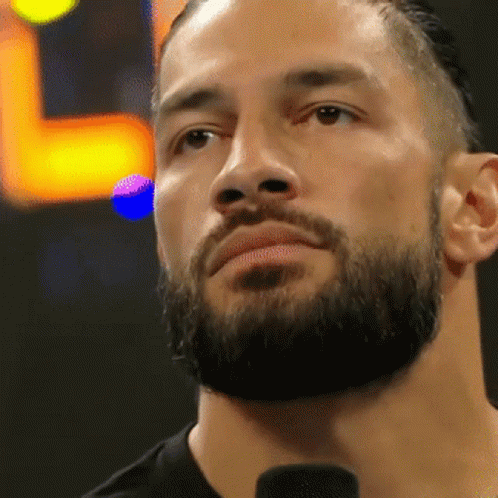 A Man With A Beard Is Standing In Front Of A Microphone And Looking At The Camera . GIF