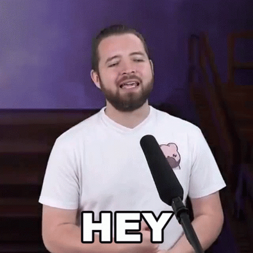 A Man With A Beard Is Standing In Front Of A Microphone And Saying Hey . GIF