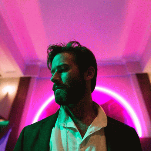 A Man With A Beard Is Standing In Front Of A Purple And Green Light GIF