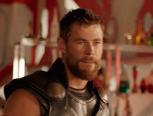 A Man With A Beard Is Standing In Front Of A Shelf With Bottles On It GIF