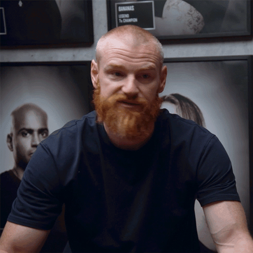 A Man With A Beard Is Standing In Front Of A Sign That Says ' Gnarmac ' On It GIF