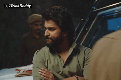 A Man With A Beard Is Standing In Front Of A Sign That Says X7wickreddy GIF