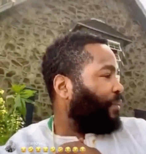 A Man With A Beard Is Standing In Front Of A Stone Building And Making A Funny Face . GIF