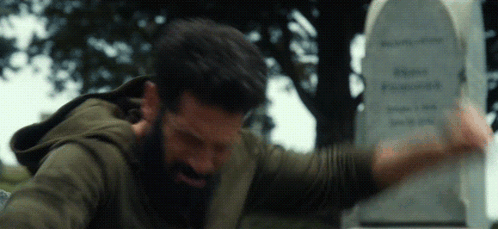 A Man With A Beard Is Standing In Front Of A Tombstone GIF