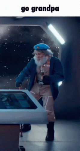 A Man With A Beard Is Standing In Front Of A Touchscreen With The Words Go Grandpa Below Him GIF