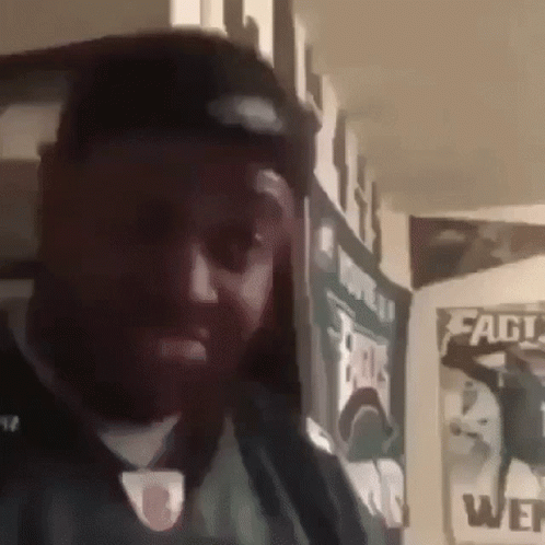 A Man With A Beard Is Standing In Front Of A Wall With A Banner That Says Eagles On It . GIF