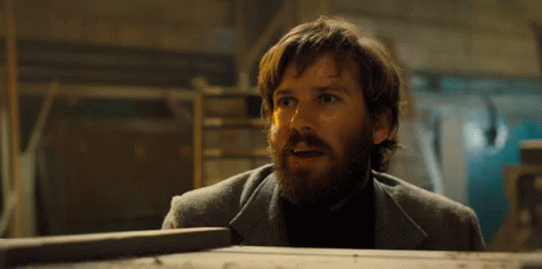 A Man With A Beard Is Standing Next To A Wooden Box And Making A Surprised Face . GIF
