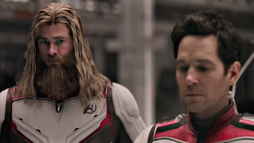 A Man With A Beard Is Standing Next To Another Man With Long Hair . GIF