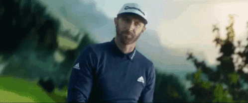 A Man With A Beard Is Standing On A Golf Course Holding A Golf Club . GIF