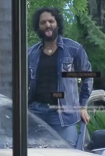 A Man With A Beard Is Sticking His Tongue Out In Front Of A Sign That Says Open GIF