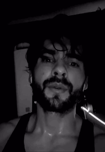A Man With A Beard Is Sweating In A Black Tank Top . GIF