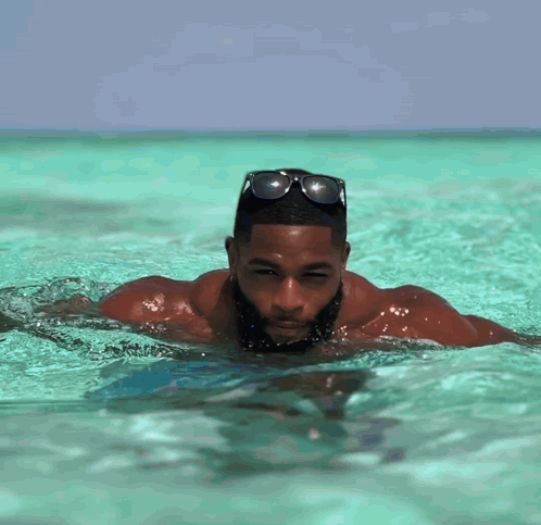 A Man With A Beard Is Swimming In The Ocean Wearing Sunglasses GIF