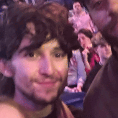 A Man With A Beard Is Taking A Selfie With Another Man In A Crowd Of People . GIF