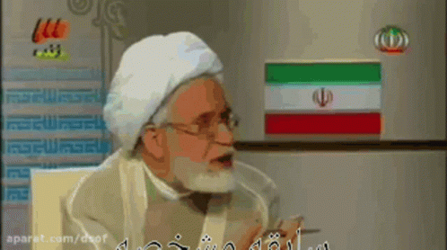 A Man With A Beard Is Talking In Front Of A Refrigerator GIF