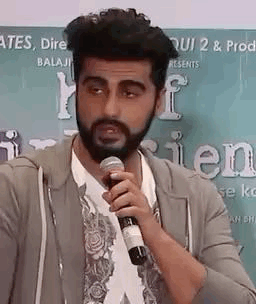 A Man With A Beard Is Talking Into A Microphone . GIF