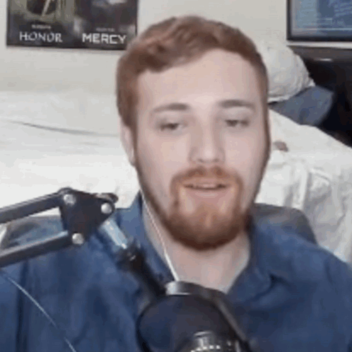 A Man With A Beard Is Talking Into A Microphone In A Room . GIF