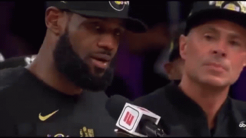A Man With A Beard Is Talking Into A Microphone While Another Man Watches . GIF
