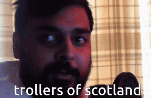A Man With A Beard Is Talking Into A Microphone With The Words " Trollers Of Scotland " Written Below Him GIF