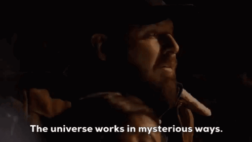 A Man With A Beard Is Talking On A Cell Phone In A Dark Room With The Words `` The Universe Works In Mysterious Ways '' GIF
