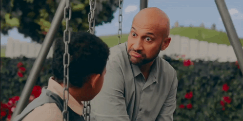 a man with a beard is talking to a boy on a swing set