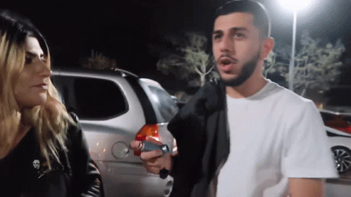 A Man With A Beard Is Talking To A Woman With A Skull On Her Jacket GIF