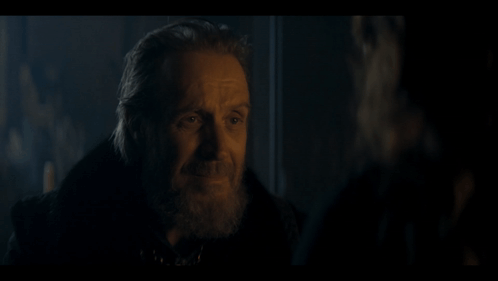 a man with a beard is talking to another man in a dark room .